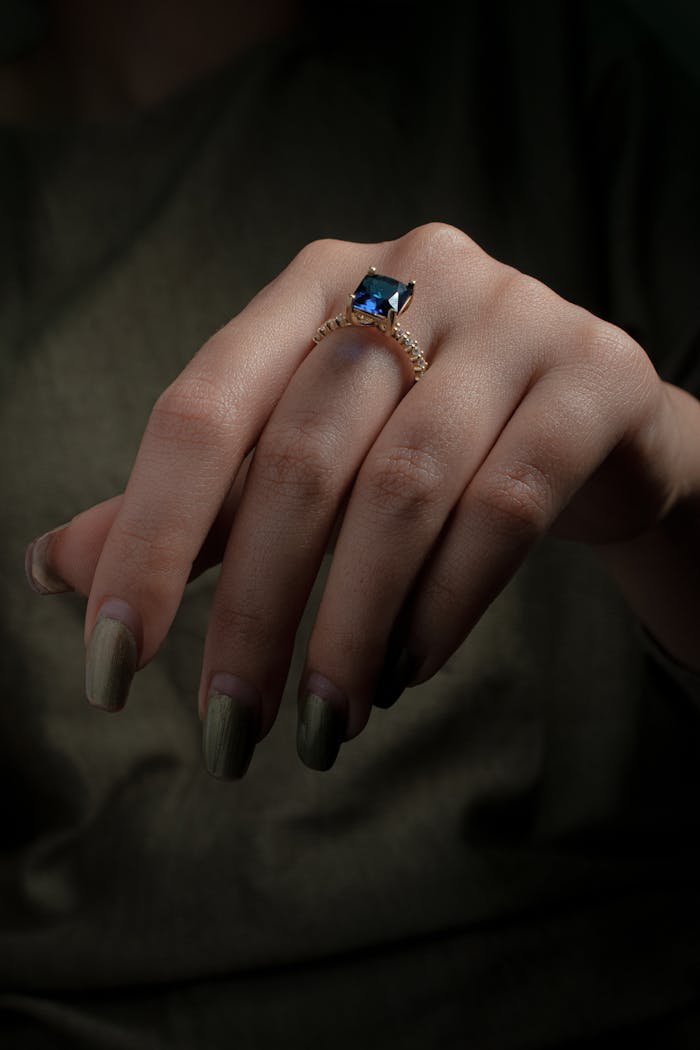 Close-up of a sapphire ring with manicured nails, symbolizing luxury and elegance.